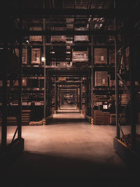 A warehouse aisle lined with racking full of stored equipment and pallets